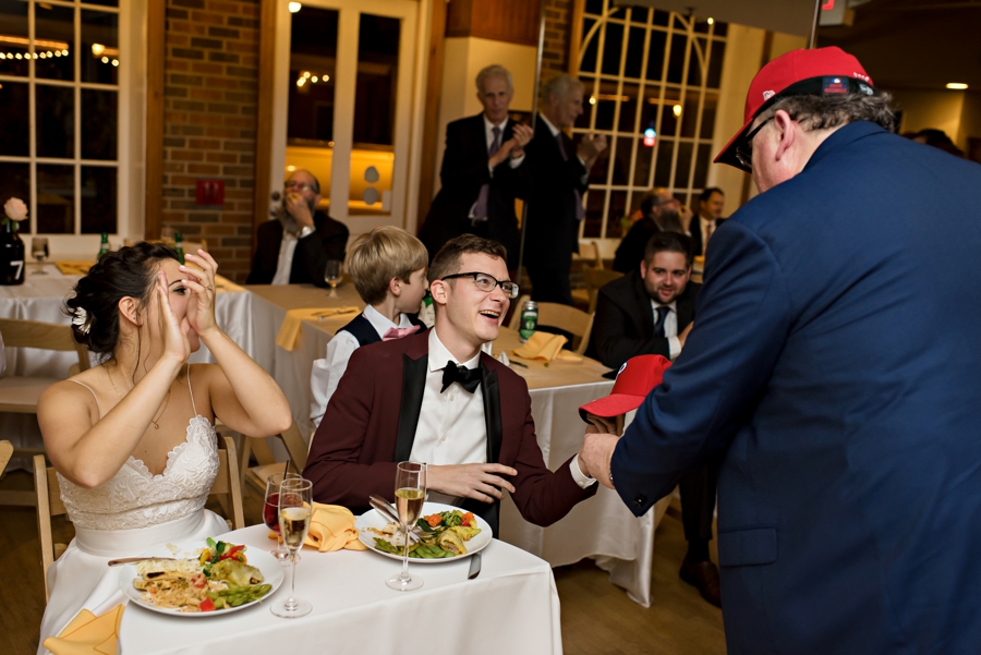 A father in law giving a Phillies hat to the groom at a reception.